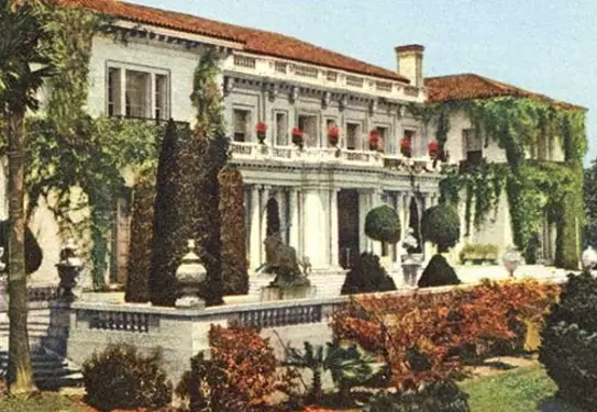 A color photo of a 1920s mansion with a manicured lawn.